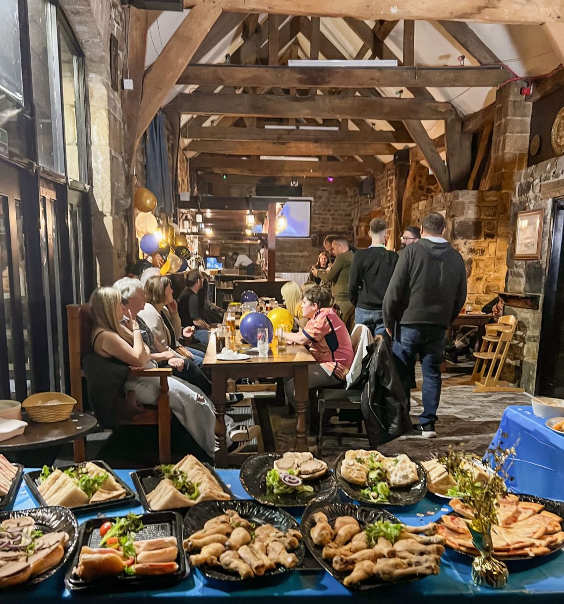 Catering Service A rustic dining setting with people enjoying food and drinks at wooden tables.